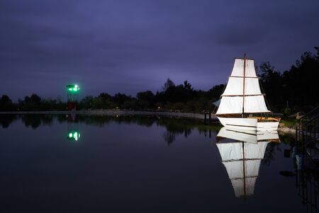 White sailboat on Lake at night. Sailboat sails on the lake with beautiful forest trees landscape. Travel background conceptの写真素材