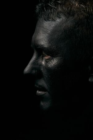 Makeup portrait of a young man with black face, close-up. Coal miner portrait isolated on dark background with copy spaceの写真素材
