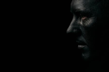 Makeup portrait of a young man with black face, close-up. Coal miner portrait isolated on dark background with copy spaceの写真素材