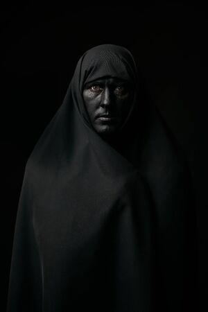 Halloween portrait of young man with black face painted. Man wearing black hijab over dark background with copy spaceの写真素材