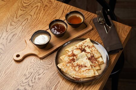 Set of pancakes with different sauces. Homemade pancakes with jam, honey and sour cream bowls, close-up.Traditional pancakes on wood table backgroundの写真素材