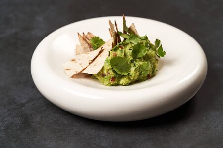 Guacamole with pita chips on white plate. Chef's signature dish, luxury gastro cafe menu food on dark background with copy space. Mexican guacamole dish.の写真素材