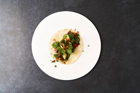 Mexican tacos with beef, tomatoes, avocado, chilli and onion on white plate background with copy...