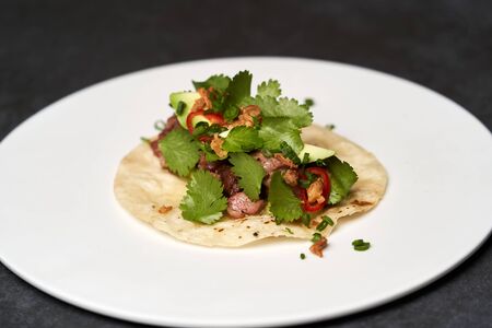 Mexican tacos with beef, tomatoes, avocado, chilli and onion on white plate background with copy...