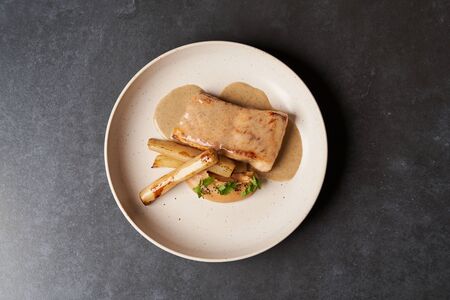 Baked Sturgeon fillet with spinach on a white plate on gray table