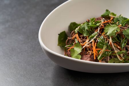 Thai style warm soba salad in white bowl on gray table background with copy space, close up