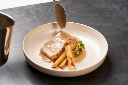 Baked Sturgeon fillet with spinach on a white plate on gray table