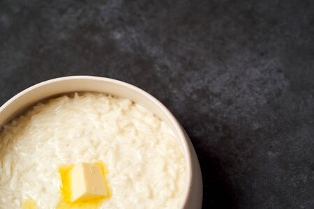 Rice porridge with milk, raisins, honey and nuts in a bowl. Healthy breakfast - milk rice porridge in a white plate on grey table background, close-upの写真素材