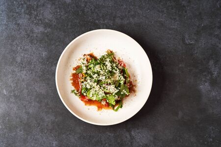 Healthy vegetable salad with grated cheese, close-up. Fresh vegetable salad in a white plate on dark table background with copy space. Healthy vegetarian foodの写真素材