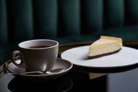 Cup of tea and slice of cheesecake on white plate on table, close-up.の写真素材
