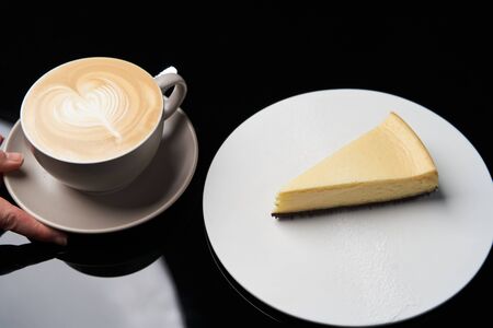Cup of tea and slice of cheesecake on white plate on table, close-up.
