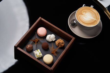 Cup of cappuccino coffee and chocolate candy in wooden box on table, close-up.の写真素材