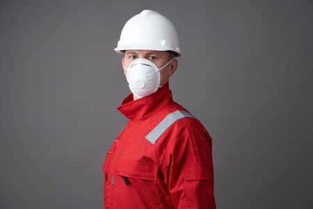 Young engineer worker wear a helmet, face mask and protective workwear suit. Worker man wearing hygienic mask, overall and protective hard hat. Coronavirus pandemic quarantine hygiene, Safety firstの写真素材