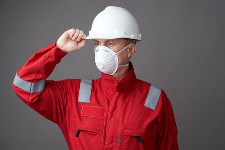 Worker man wearing hygienic mask, overall and protective hard hat. Young engineer worker wear a...