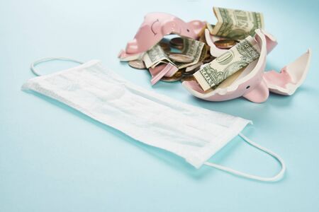 Medical mask and broken piggy bank with coins money on blueの写真素材