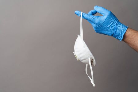 Coronavirus prevention concept. Hand with latex glove and medical mask. Doctor's hand with medical face mask and protective glove on gray background with copy space, close-upの写真素材