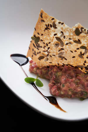 Fresh beef tartar with whole grain chips. Raw tartar meat in white plate on tableの写真素材