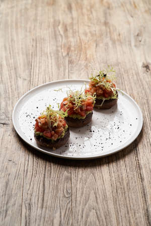 Salmon tartare with guacamole sauce. Toasts with guacamole and salmon on white plate. Luxury...