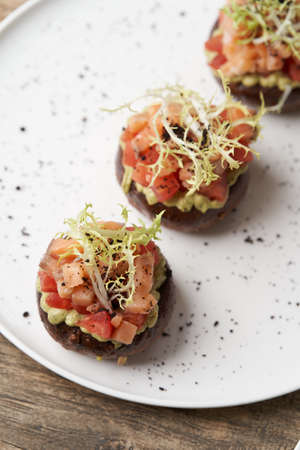 Salmon tartare with guacamole sauce. Toasts with guacamole and salmon on white plate. Luxury restaurant food tableの写真素材