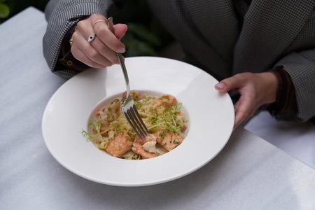 Woman eating Fettuccine pasta with shrimp and cheese. Italian pasta fettuccine on a white plate on the tableの写真素材