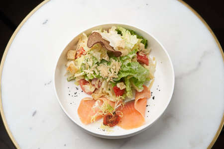 Caesar salad with salmon fish on white bowl. Seafood caesar salad on table, close-upの写真素材