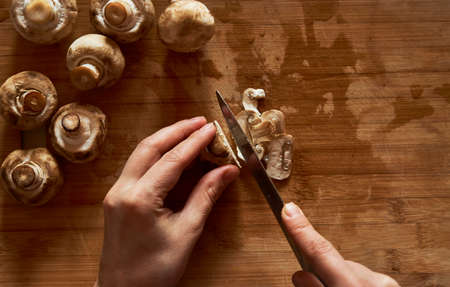 Woman cutting mushrooms on wooden board, close-up. Woman hands with knife chopping mushroom
