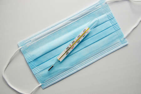 Checking body temperature concept. Medical mask and thermometer, close-up. Glass mercury thermometer...
