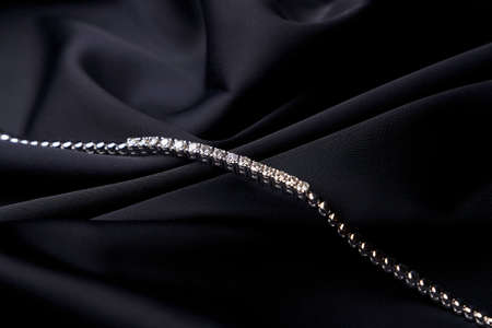 Platinum bracelet with diamonds on black silk background. White gold bracelet with gemstones, close-up. Elegant woman jewelryの写真素材