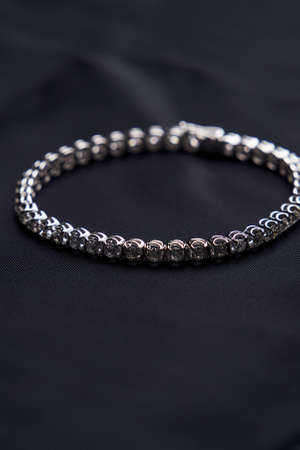 Platinum bracelet with diamonds on black silk background. White gold bracelet with gemstones, close-up. Elegant woman jewelryの写真素材