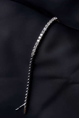 Platinum bracelet with diamonds on black silk background. White gold bracelet with gemstones, close-up. Elegant woman jewelryの写真素材