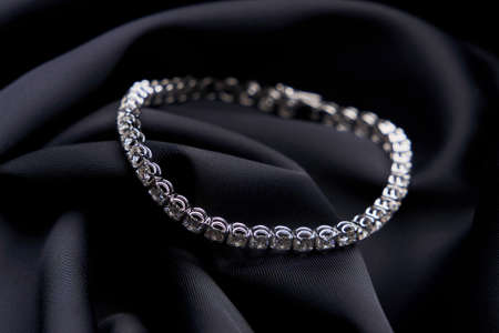 Platinum bracelet with diamonds on black silk background. White gold bracelet with gemstones, close-up. Elegant woman jewelryの写真素材