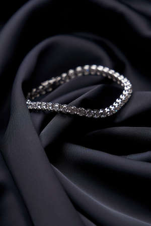Platinum bracelet with diamonds on black silk background. White gold bracelet with gemstones, close-up. Elegant woman jewelryの写真素材
