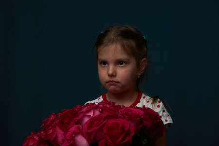 Little girl with a flowers bouquet. Cute baby girl with bouquet of roses flowers on dark background...
