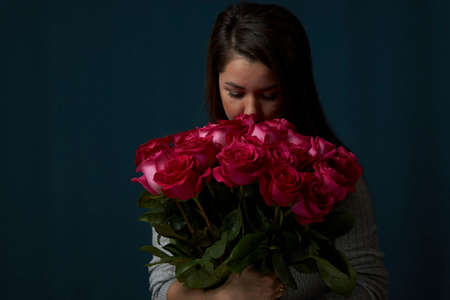 Beautiful woman with a flowers bouquet. Young woman holding bouquet of roses flowers on dark...