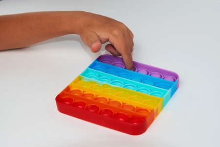 Child with poppit toy on a white background, close-up. Finger push colorful poppit game. Silicone Tie-dye Push pop Bubbleの写真素材