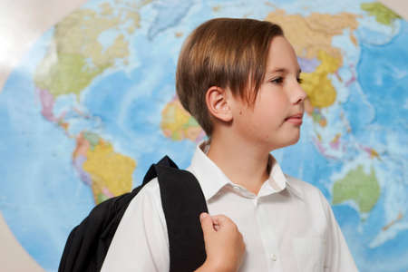 School boy with a backpack. Portrait of a boy with school bag on blue map background, close-up. Back to school and education conceptの写真素材