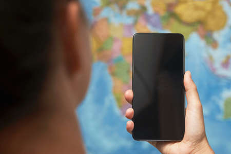 Woman hand holding phone on blue map background with copy space. Woman holding smartphone with black screen. Hand with blank cellphone display, close-up. Travel conceptの写真素材