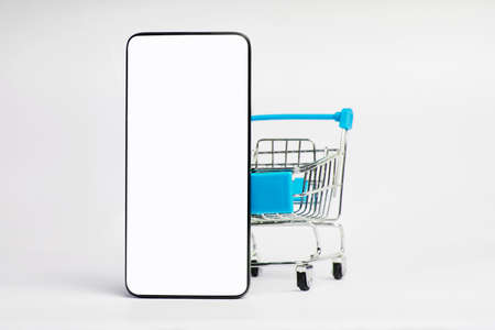 Shopping cart and mobile phone isolated on white background with copy space. Blank smartphone screen...