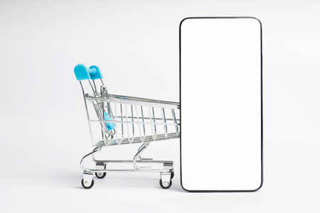 Shopping cart and mobile phone isolated on white background with copy space. Blank smartphone screen...