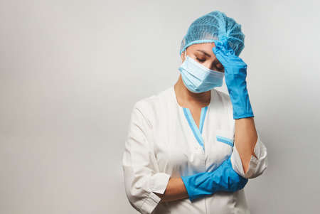 Exhausted female doctor having headache. Portrait of a woman nurse having headache. Covid 19, coronavirus concept.の写真素材