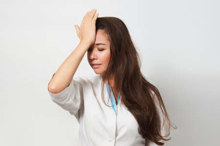 Exhausted female doctor having headache. Portrait of a woman nurse having headache. Covid 19, coronavirus concept.の写真素材
