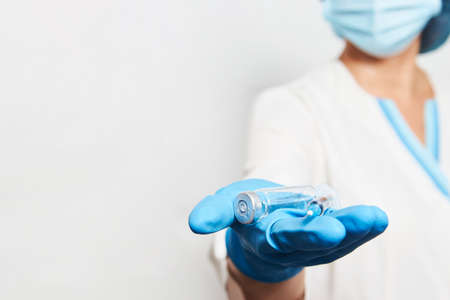 Woman doctor with vaccine bottle. Portrait of a female doctor in safety mask and gloves holds bottle with liquid medicine for injectionsの写真素材
