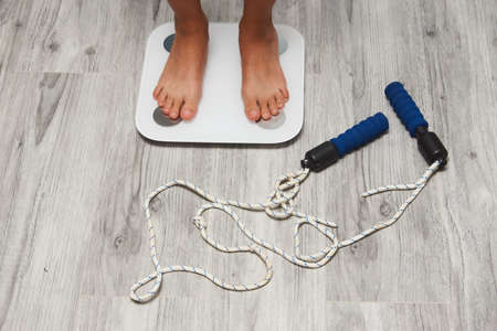 Female leg stepping on floor scales, close-up. Woman and weighing scales at home. Diet, healthy lifestyle, loss weight, slim concept.の写真素材