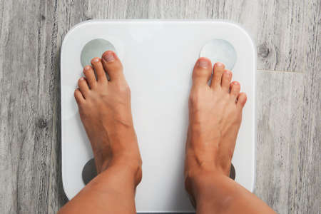 Female leg stepping on floor scales, close-up. Woman and weighing scales at home. Diet, healthy lifestyle, loss weight, slim concept.の写真素材