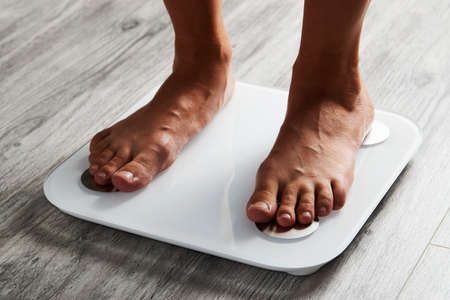 Female leg stepping on floor scales, close-up. Woman and weighing scales at home. Diet, healthy...