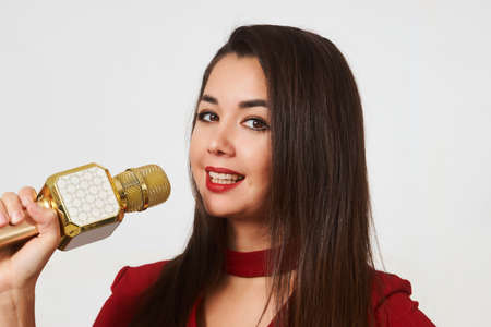 Young woman holding microphone, close-up. Portrait of young woman singing karaoke. Beautiful girl with microphone on white backgroundの写真素材