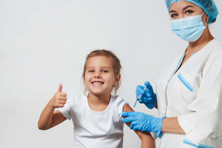 The concept of vaccination. Female doctor injecting vaccine to girl. Young nurse doctor and child girl on white background with copy space, close-upの写真素材