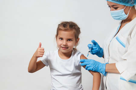 The concept of vaccination. Female doctor injecting vaccine to girl. Young nurse doctor and child girl on white background with copy space, close-upの写真素材