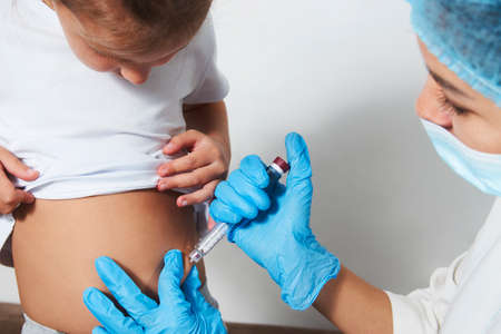Diabetes in children concept. Girl getting insulin by female doctor. Doctor inject insulin pen to child girl on white background with copy space.の写真素材
