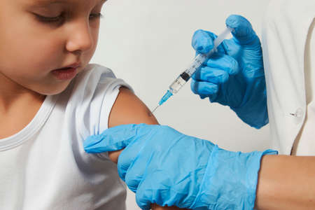 The concept of vaccination. Female doctor injecting vaccine to girl. Young nurse doctor and child girl on white background with copy space, close-upの写真素材